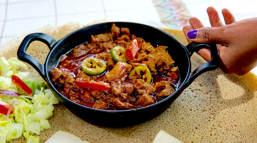 Sizzling beef tibs being seared in a traditional clay cooking pot, known as a shekla at Habesha Cafe.